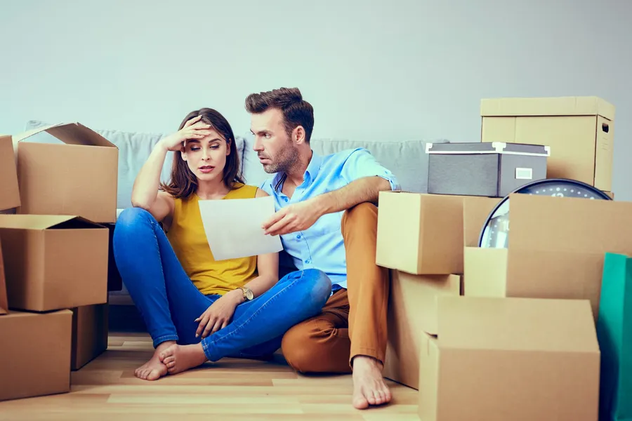 A couple sitting on the floor surrounded by moving boxes holding a lease document