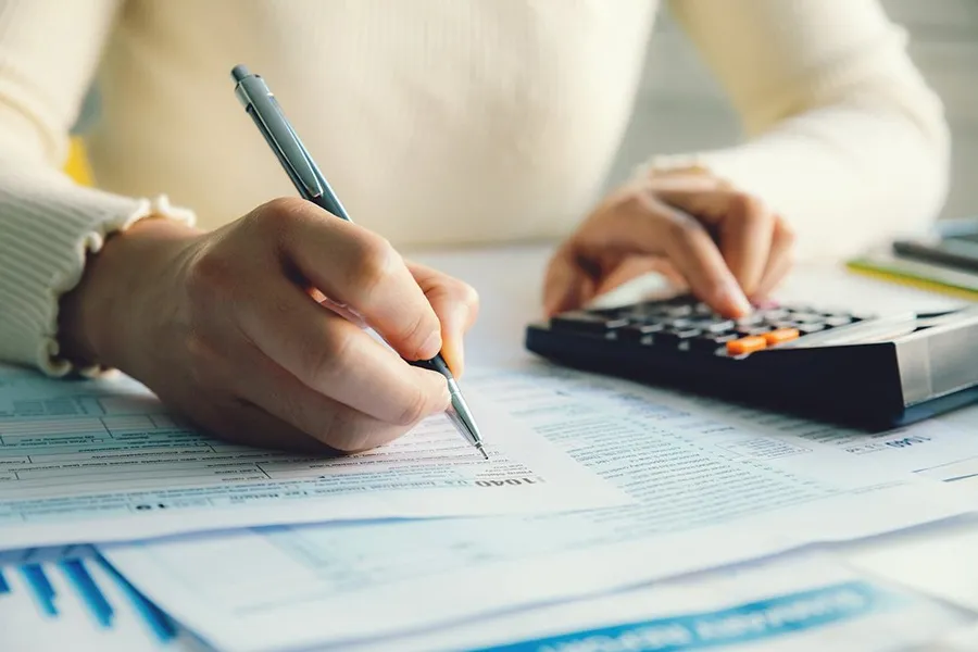 Woman with a pencil writing on a bill while punching in numbers on a calculator