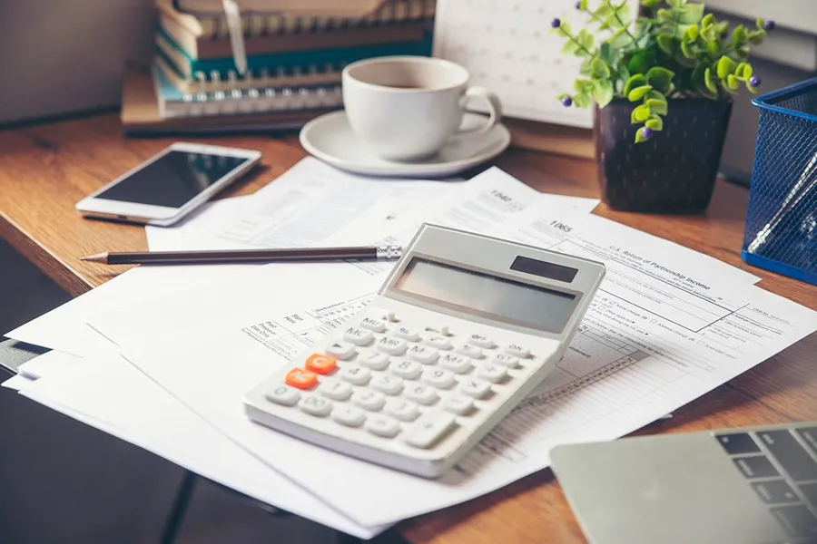 A desk with documents, calculator, pencil, cup of coffee and phone
