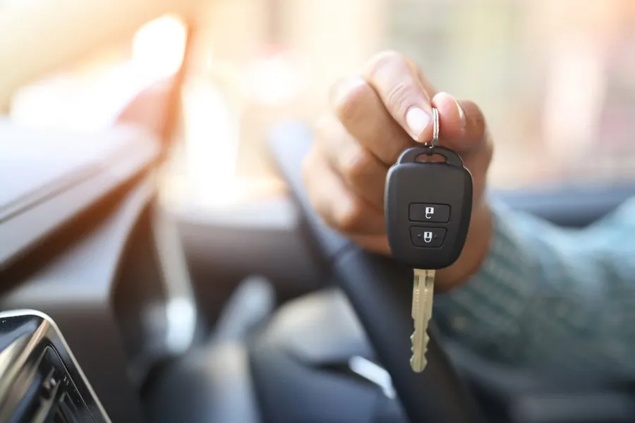 A hand holds a car key inside a car, with the vehicle's interior visible in the background, contemplating a looming repossession