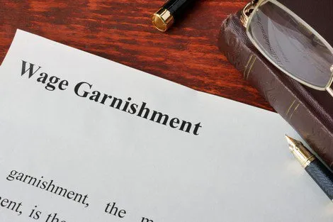 A document titled "Wage Garnishment" with glasses and a pen on a desk.