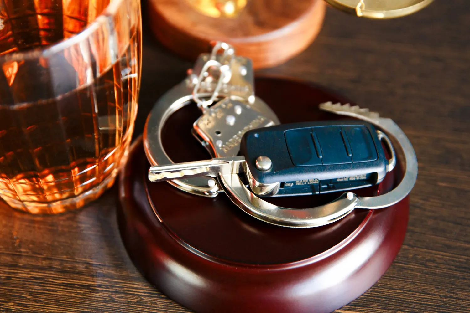 Car keys and a handcuff on a table next to a glass of whiskey indicating a DUI.