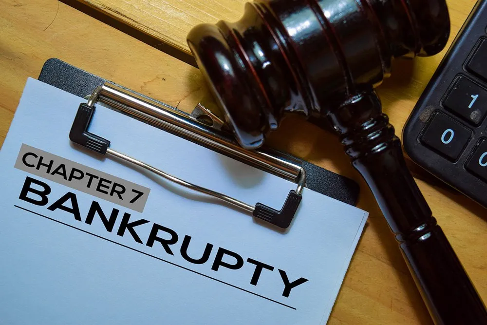 A clipboard with a document labeled "Bankruptcy Chapter 7" is next to a judge's gavel and a portion of a keyboard.