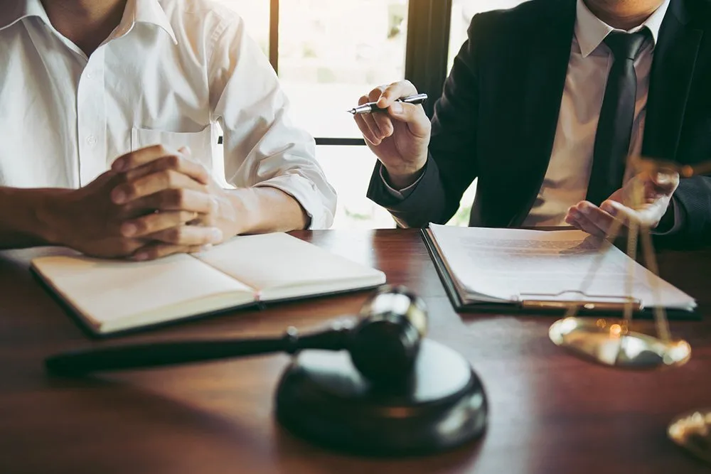 Two professionals at a desk with documents, a gavel, and legal scales, suggesting a legal setting.