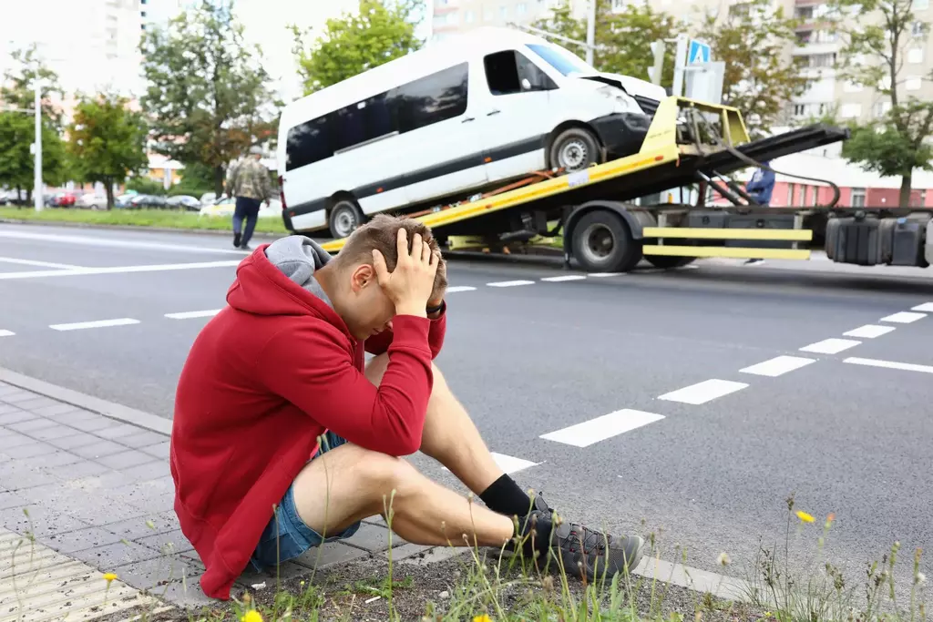 Man sitting on ground beside a tow truck with his vehicle being repossessed