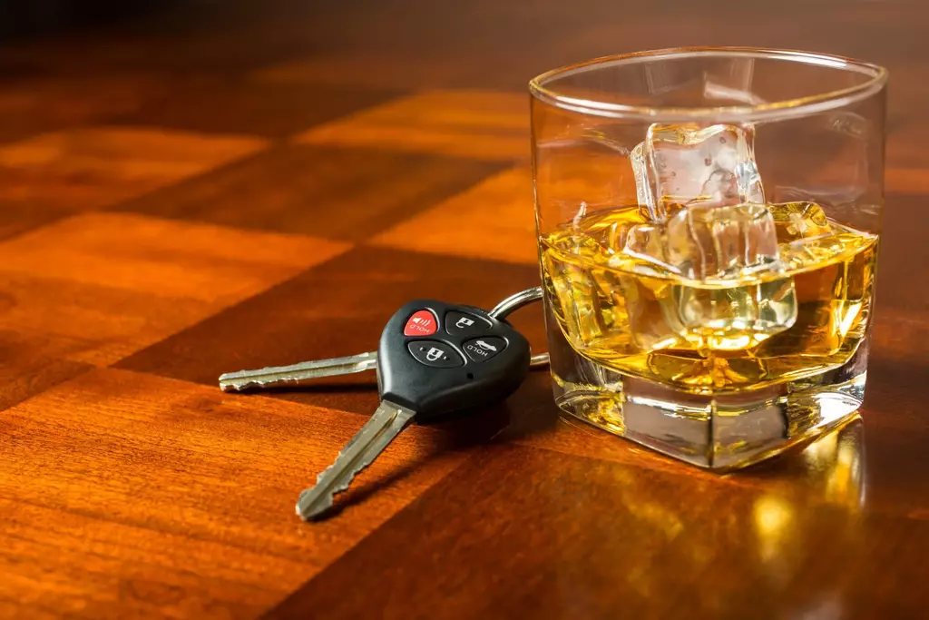 A glass containing whiskey and a set of car keys sitting on a table