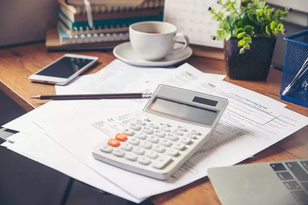 Desk with a tax return, calculator, cup of coffee, pencil and a plant