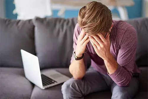 A man is seated on a couch, with his head in his hands, reflecting feelings of sadness or overwhelming thoughts over his divorce and financial distress.