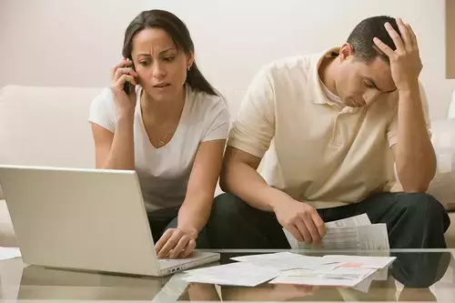 A couple sits together with a laptop and scattered papers, discussing their impending bankruptcy filing.