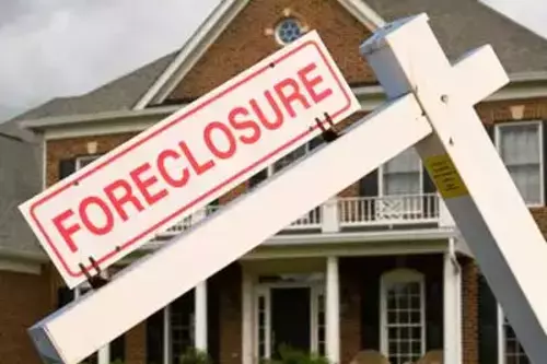 A foreclosure sign stands in front of a house, highlighting the property’s status as being in foreclosure.